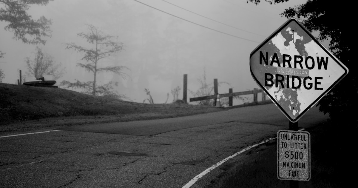 Narrow bridge warning sign on a foggy road